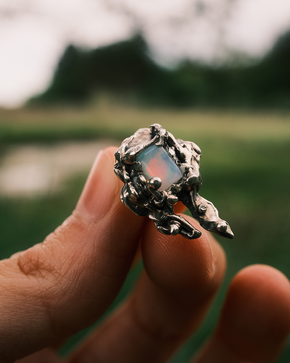 Boucle d’oreille organique en argent massif avec opale tenue entre les doigts