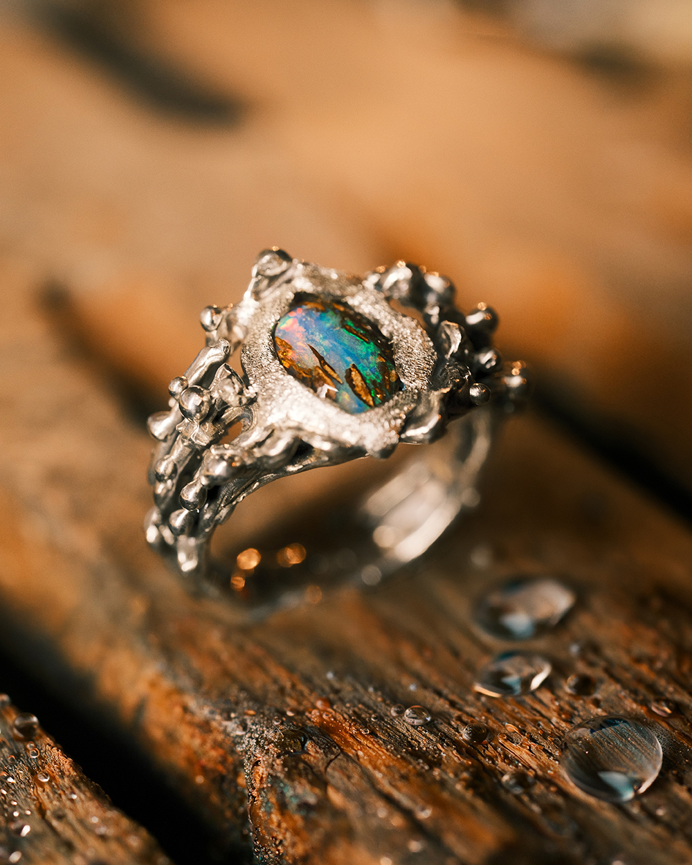 Opale boulder naturelle - Jungle Aquatique Gros plan sur une opale boulder aux reflets bleus verts et orangés sertie dans une bague artisanale en argent