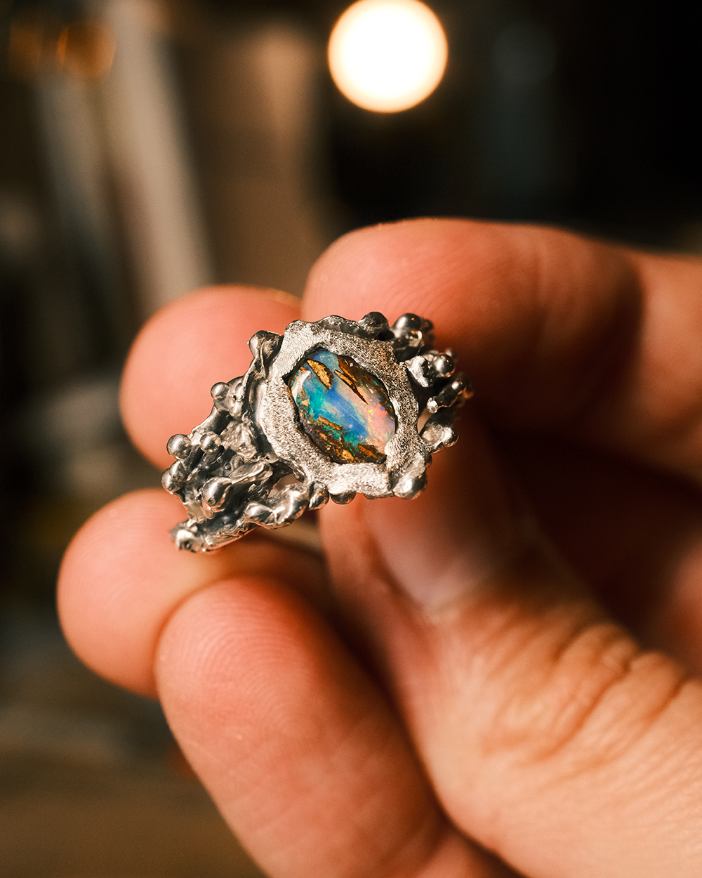 Jungle Aquatique - détail de la bague artisanale Bague artisanale organique en argent 925 avec opale boulder tenue entre les doigts